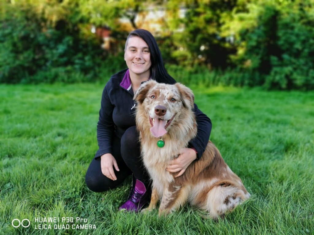 A woman crouching down with her dog in the grass.