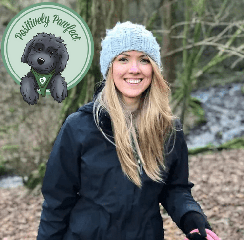 A woman in a blue jacket standing in a wooded area with a black poodle, providing rehabilitation support