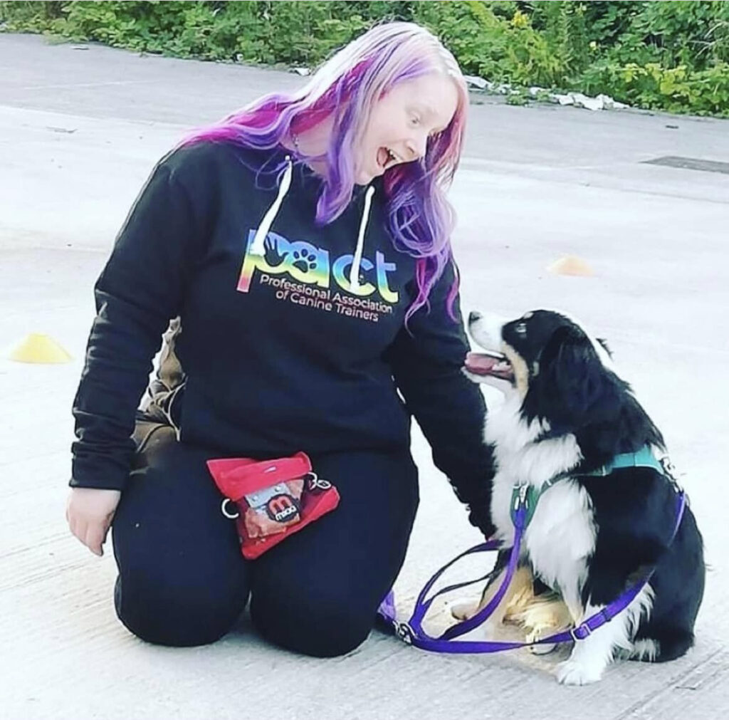 A woman with purple hair coaching a dog.